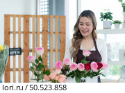 ?Young woman florist smelling a red rose in the flower shop. Стоковое фото, агентство Ingram Publishing / Фотобанк Лори
