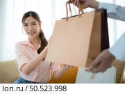 The receptionist delivers the goods that the customer has already purchased to Asian women on the sofa with shopping bags. Стоковое фото, агентство Ingram Publishing / Фотобанк Лори
