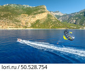 Aerial view of parasailing on the blue sea in Oludeniz, Turkey. Top view of speed boat, water and people with parasail, mountains, beach at sunset in summer. Extreme vacation. Sport. Travel. Стоковое фото, агентство Ingram Publishing / Фотобанк Лори