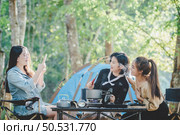 Young asian woman cooking and her friend enjoy to make the meal in pot, They are talk and laugh with fun together while camping in nature park. Стоковое фото, агентство Ingram Publishing / Фотобанк Лори