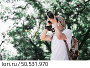 Asian traveler man with backpack taking a photo in the park with copy space. Travel photographer. Vocation and holiday concept. Стоковое фото, агентство Ingram Publishing / Фотобанк Лори