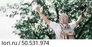 Asian traveler man with backpack holding a camera and making a happy gesture in forest with copy space. Travel photographer. Vocation, suscess and holiday concept. Стоковое фото, агентство Ingram Publishing / Фотобанк Лори