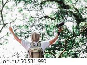 Asian traveler man with backpack holding a camera and making a happy gesture in forest with copy space. Travel photographer. Vocation, suscess and holiday concept. Стоковое фото, агентство Ingram Publishing / Фотобанк Лори