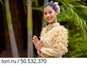 Young pretty woman dressed in beautiful Thai costumes, standing with hands folded in respect in temple on Songkran festival. Thai New Year, Family Day in April. Стоковое фото, агентство Ingram Publishing / Фотобанк Лори