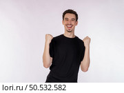 Portrait of happy joyful young man standing doing winner gesture clenching fists keeping isolated on white color wall background studio. Victory and success concept. Стоковое фото, агентство Ingram Publishing / Фотобанк Лори
