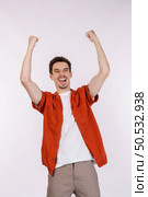 Portrait of happy joyful young man standing doing winner gesture clenching fists keeping isolated on white color wall background studio. Victory and success concept. Стоковое фото, агентство Ingram Publishing / Фотобанк Лори