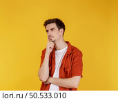 Portrait of young man thinking touching chin isolated over yellow background. Thinking worried about a question, concerned and nervous with hand on chin. Стоковое фото, агентство Ingram Publishing / Фотобанк Лори