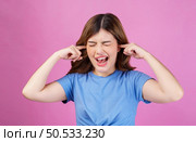 Portrait of angry irritated young woman wearing casual t-shirt covering her ears with hands and shouting while standing isolated over pink background. Expression, people and lifestyle concept. Стоковое фото, агентство Ingram Publishing / Фотобанк Лори
