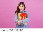 Portrait of Excited surprised young woman holding gift in her hands isolated over pink background. Birthday and celebration concept. Стоковое фото, агентство Ingram Publishing / Фотобанк Лори