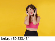Portrait of Happy young woman listening music in headphones and singing while standing isolated over yellow background. Lifestyle and entertainment concept. Стоковое фото, агентство Ingram Publishing / Фотобанк Лори