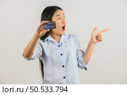Portrait of positive young asian woman showing credit card good mood salary and pointing finger at aside isolated on white background. Finance, currency, payment and people concept. Стоковое фото, агентство Ingram Publishing / Фотобанк Лори