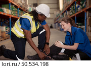 A warehouse worker consoles and helps a female worker who cries out in pain after a leg accident in a large warehouse. Стоковое фото, агентство Ingram Publishing / Фотобанк Лори