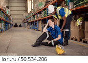 A warehouse worker consoles and helps a female worker who cries out in pain after a leg accident in a large warehouse. Стоковое фото, агентство Ingram Publishing / Фотобанк Лори