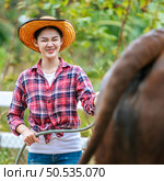 Portrait of Happy young Asian farmer woman wearing hat working to clean cow in farm. Agriculture industry, farming, people, technology and animal husbandry concept. Стоковое фото, агентство Ingram Publishing / Фотобанк Лори