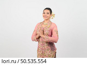 Young beautiful woman dress in local culture in southern region in thailand with gesture put hands together when greeting and welcome or while saying thank you, looking camera and smile, copy space. Стоковое фото, агентство Ingram Publishing / Фотобанк Лори