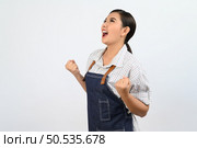 Portrait Asian young woman in waitress uniform and apron shouting and raised hands with happy in success on white background, copy space for advertising . Стоковое фото, агентство Ingram Publishing / Фотобанк Лори