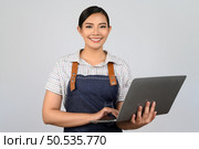 Portrait of young asian woman in waitress uniform holding a laptop computer posture, copy space to insert products for advertisement isolated on white background. Стоковое фото, агентство Ingram Publishing / Фотобанк Лори