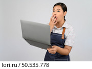Portrait of young asian woman in waitress uniform looking on laptop computer monitor with feel surprise posture, copy space to insert products for advertisement isolated on white background. Стоковое фото, агентство Ingram Publishing / Фотобанк Лори