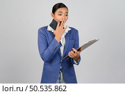 Portrait Asian young woman in officer uniform standing with mobile phone and report paper on clipboard in hand posture,  isolated on white background. Стоковое фото, агентство Ingram Publishing / Фотобанк Лори