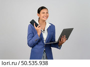 Portrait Asian young woman in officer uniform standing posture talking with mobile phone during working with laptop computer in hand with feel exciting,  isolated on white background. Стоковое фото, агентство Ingram Publishing / Фотобанк Лори