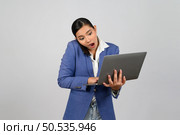 Portrait Asian young woman in officer uniform standing posture talking with mobile phone during working with laptop computer in hand with feel exciting,  isolated on white background. Стоковое фото, агентство Ingram Publishing / Фотобанк Лори