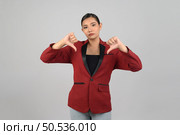 Portrait Asian young woman in officer uniform standing showing thumb down posture, Pretty girl grimace with dissatisfaction and make hand thumb down gestures, isolated on white background. Стоковое фото, агентство Ingram Publishing / Фотобанк Лори