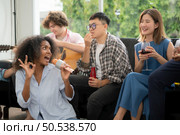 Group of multiethnic friends having fun at party by playing guitar and singing together at home. Стоковое фото, агентство Ingram Publishing / Фотобанк Лори