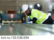 Young engineers engineers testing and confirming that the machinery at the factory that creates metal sheet tiles is functioning as intended. Стоковое фото, агентство Ingram Publishing / Фотобанк Лори