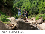Young man hiker with backpack and trekking poles with a young man helping to pull him up to stand on the rock. Стоковое фото, агентство Ingram Publishing / Фотобанк Лори