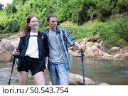 Young woman hiker with backpack and trekking poles with a young man helping to pull him up to stand on the rock. Стоковое фото, агентство Ingram Publishing / Фотобанк Лори
