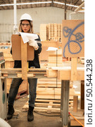 Female carpenter working in a woodworking factory, She is wearing a safety helmet and glasses. Checking the neatness of the planks against the design documents. Стоковое фото, агентство Ingram Publishing / Фотобанк Лори