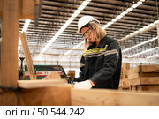 Female carpenter working in a woodworking factory, She is wearing a safety helmet and glasses. Checking the neatness of the planks against the design documents. Стоковое фото, агентство Ingram Publishing / Фотобанк Лори