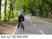 Young woman listening to music with headphones while biking in the park. Стоковое фото, агентство Ingram Publishing / Фотобанк Лори