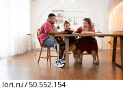 A plus-size family with a father wearing a prosthetic leg, is happily assisting a child with her homework and having fun together in the dining room of the house before cooking together. Стоковое фото, агентство Ingram Publishing / Фотобанк Лори