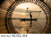 Silhouette of fisherman at sunrise, Standing aboard a rowing boat and casting a net to catch fish for food. Стоковое фото, агентство Ingram Publishing / Фотобанк Лори