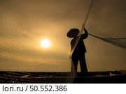 Silhouette of fisherman at sunrise, Standing aboard a rowing boat and casting a net to catch fish for food. Стоковое фото, агентство Ingram Publishing / Фотобанк Лори
