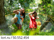 Two girls Asian women with traditional clothing stand in the rainforest. They had fun playing together before assisting Grandpa in catching fish in a nearby lake. Стоковое фото, агентство Ingram Publishing / Фотобанк Лори