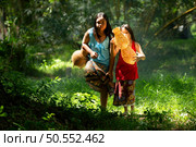 Two girls Asian women with traditional clothing stand in the rainforest. They had fun playing together before assisting Grandpa in catching fish in a nearby lake. Стоковое фото, агентство Ingram Publishing / Фотобанк Лори