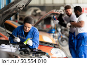 Car mechanic working in an auto repair shop, inspecting the operation of the car’s air conditioner and refrigerant, Focus on woman. Стоковое фото, агентство Ingram Publishing / Фотобанк Лори