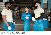 Portrait of smiling team of mechanics in auto repair shop,  Talking one another while standing under car. Стоковое фото, агентство Ingram Publishing / Фотобанк Лори
