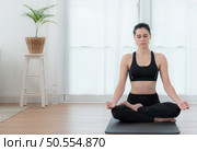 Young woman meditating in lotus pose on exercise mat at home, Yoga exercise concept. Стоковое фото, агентство Ingram Publishing / Фотобанк Лори