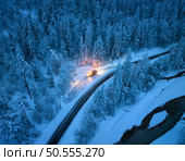 Aerial view of mountain road in fairy forest in snow and snowplow clears the snow off a road at night in winter. Top view from drone of highway, snowy pine trees, river and snow plow truck at dusk. Стоковое фото, агентство Ingram Publishing / Фотобанк Лори
