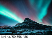 Northern lights and snowy mountains at night in Lofoten, Norway. Aurora borealis above the snow covered rocks. Winter landscape with polar lights, mountain peak. Starry sky with bright aurora. Стоковое фото, агентство Ingram Publishing / Фотобанк Лори