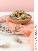 Quail eggs in a ceramic bowl with a peach fuzz pink colored scarf and bird feathers. Wooden table painted white and a plain pink background. Background with elements suggestive of the Easter season. Стоковое фото, агентство Ingram Publishing / Фотобанк Лори