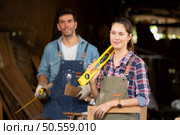 Portrait of carpenter female worker standing in front of colleague in workshop, Eyesight is utilized to ensure accuracy. Стоковое фото, агентство Ingram Publishing / Фотобанк Лори