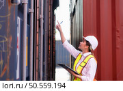 Workers in the import and export industries inspect the cargo of containers while holding a laptop and standing between them. Стоковое фото, агентство Ingram Publishing / Фотобанк Лори