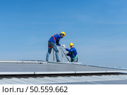 A young technician intern working on solar panels is fear of heights with senior engineers who are always helping out. Стоковое фото, агентство Ingram Publishing / Фотобанк Лори