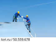 A young technician intern working on solar panels is fear of heights with senior engineers who are always helping out. Стоковое фото, агентство Ingram Publishing / Фотобанк Лори