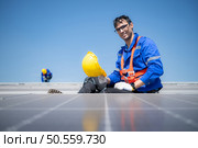 Technician repairing solar panels take off his hat and rest in the scorching sun on a factory roof covered with solar panels to receive solar energy. Стоковое фото, агентство Ingram Publishing / Фотобанк Лори