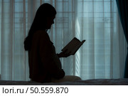 In silhouette, Pregnant woman reading a stories to her unborn child in the living room at home. Стоковое фото, агентство Ingram Publishing / Фотобанк Лори